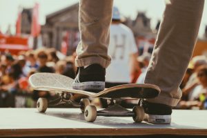 zoom sur les pieds d'un homme portant des baskets foncées et un pantalon chino beige avec un pied posé sur une skate